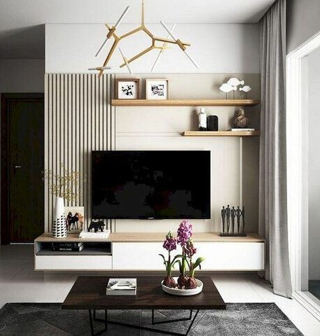 A modern living room featuring a large black tv on a white console with shelves. decor includes sculptures, books, and a potted orchid on a coffee table. a geometric ceiling light adds a unique touch.