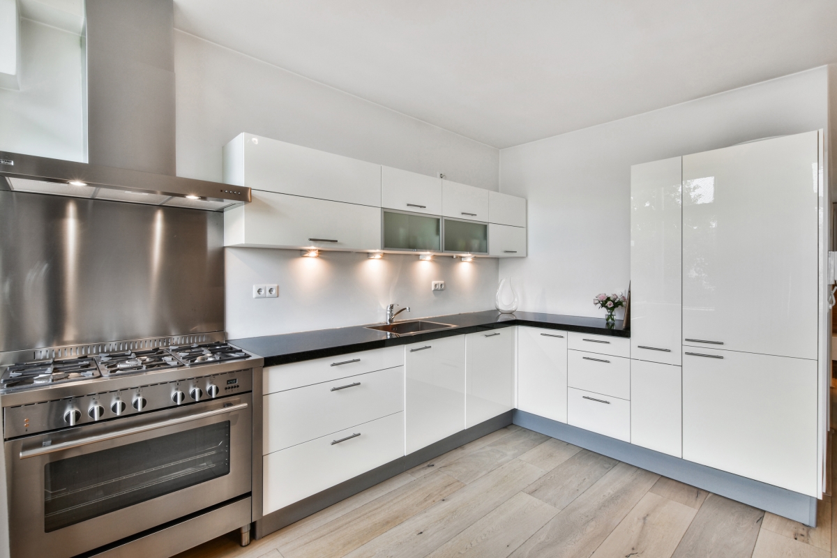 Modern kitchen with white cabinetry, black countertops, and stainless steel appliances, including a range and oven. the room features under-cabinet lighting and a light gray floor, creating a clean and sleek look.