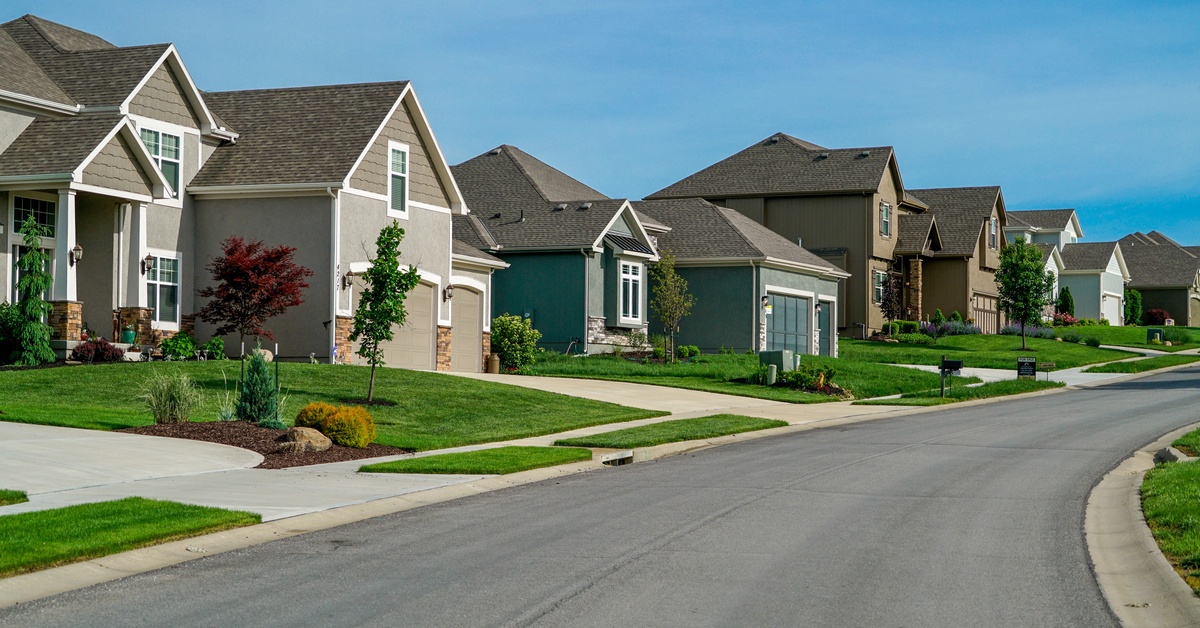 Multiple houses of different sizes and colors, aligned next to each other with a wide concrete street on the side.