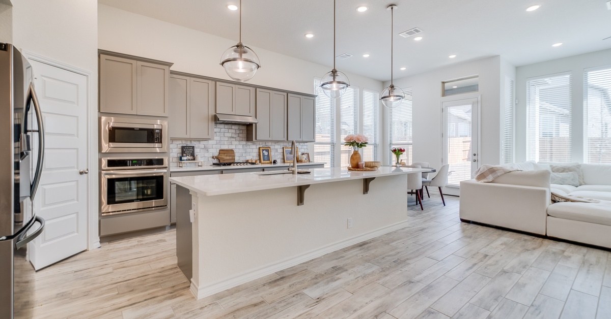 A modern kitchen with a large white counter, grey cabinets, stainless-steel appliances, and a small round dining table.