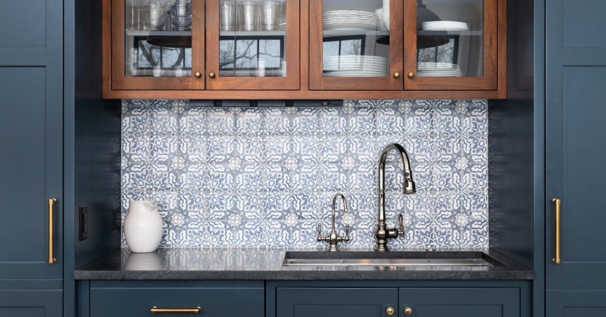 A stainless-steel faucet on a black counter under brown cabinets fill of dishes and a blue tiled backsplash.