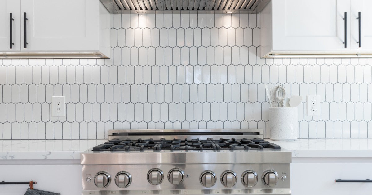 A close-up of a stainless-steel oven with an extraction vent, white cabinets, countertops, and a tiled backsplash.