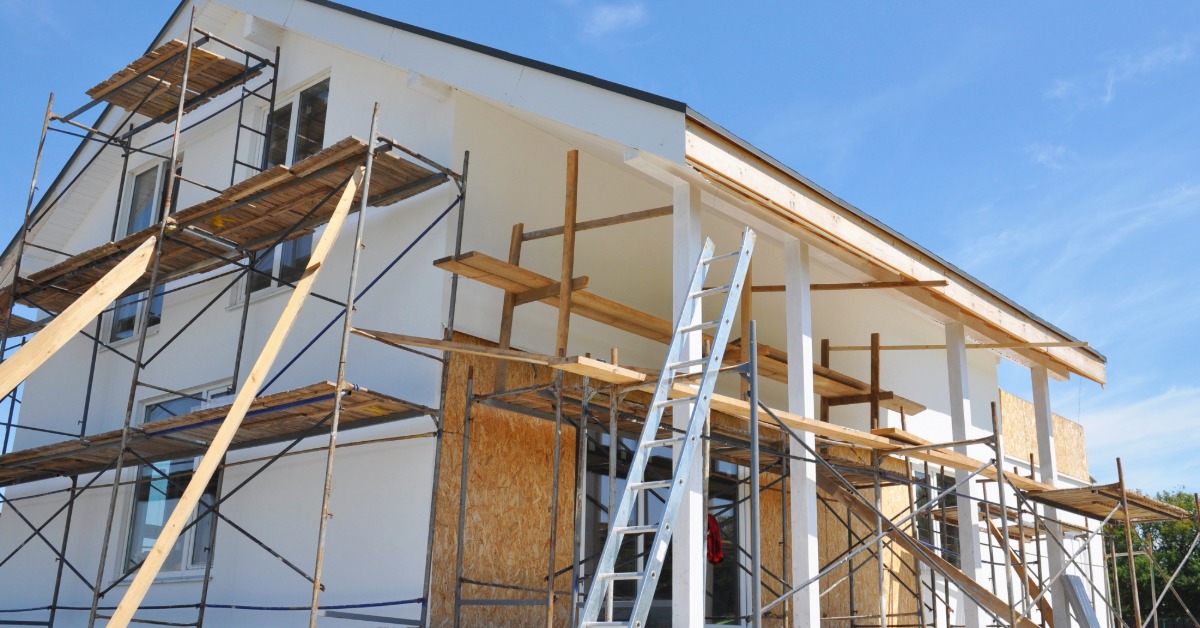 A two-story home undergoing renovations with outdoor scaffolding surrounding it, ladders, and wooden beams.