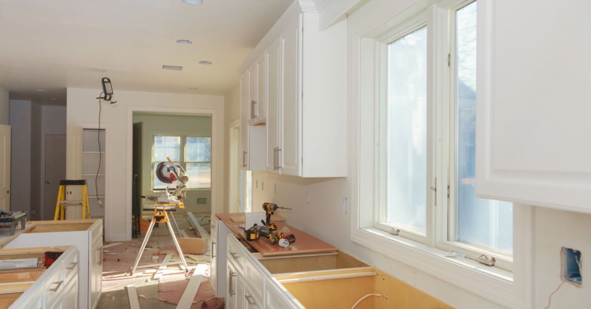 A kitchen with white cabinets and silver hardware, with a counter missing the sink, and a wood cutter in the background.