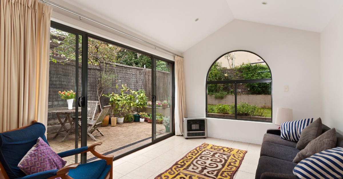 A room with large sliding window doors, white floors and walls, a couch, and a chair with an exteriors view.