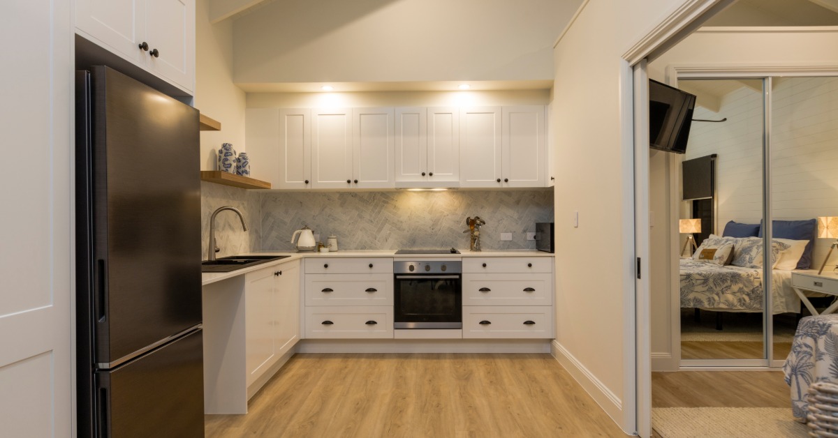 A small kitchen with a black refrigerator and white cabinets, next to a room with sliding doors and a closet.