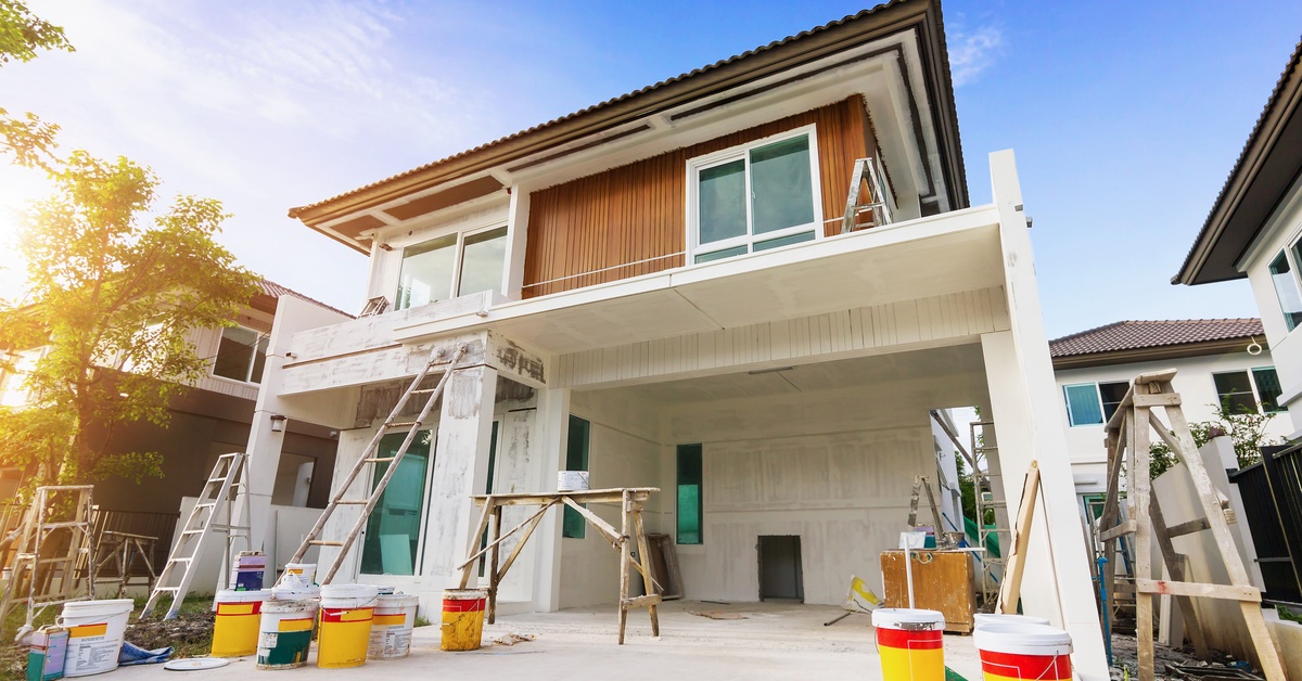 A two-story home with white walls, a ladder next to the front garage, and multiple yellow buckets on the ground.