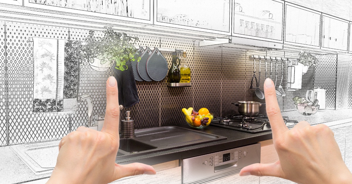 A close-up of two hands doing an L-shape to frame the center of a kitchen with color, and the rest is black and white.