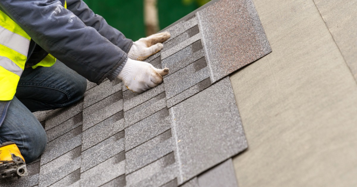 A close-up of the hands of a worker wearing white protective gloves laying a synthetic tile on the roof of a home.