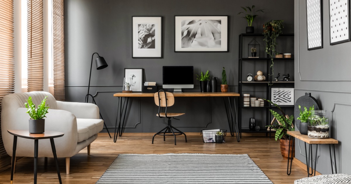 A room with wooden floors, small wooden tables with metal legs, an area rug, and a desk with a large monitor.