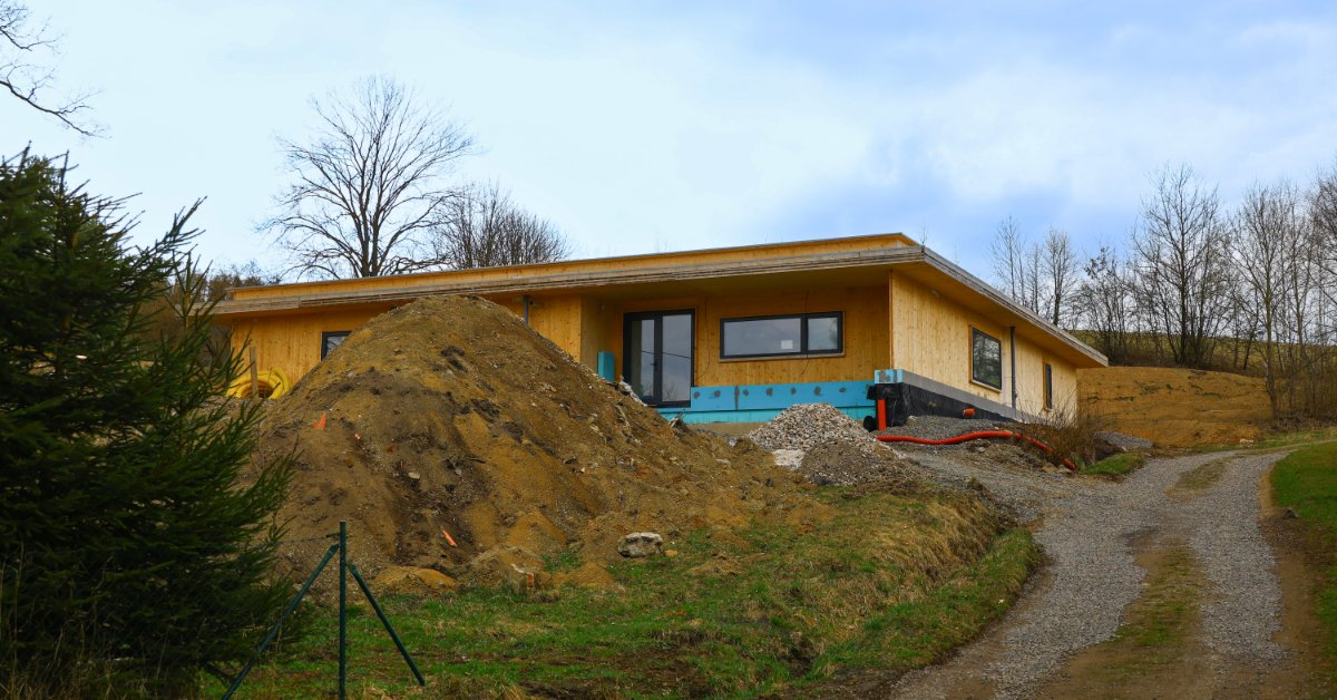 A single-story house under construction with a large pile of dirt in front, next to a sloped path covered in gravel.