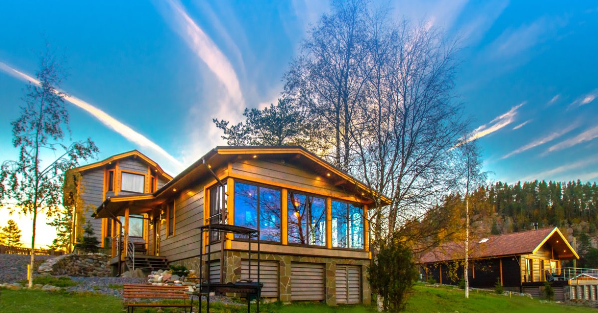 A two-story home with a casita in the back, built on uneven terrain with lush grass and trees on a sunny day.