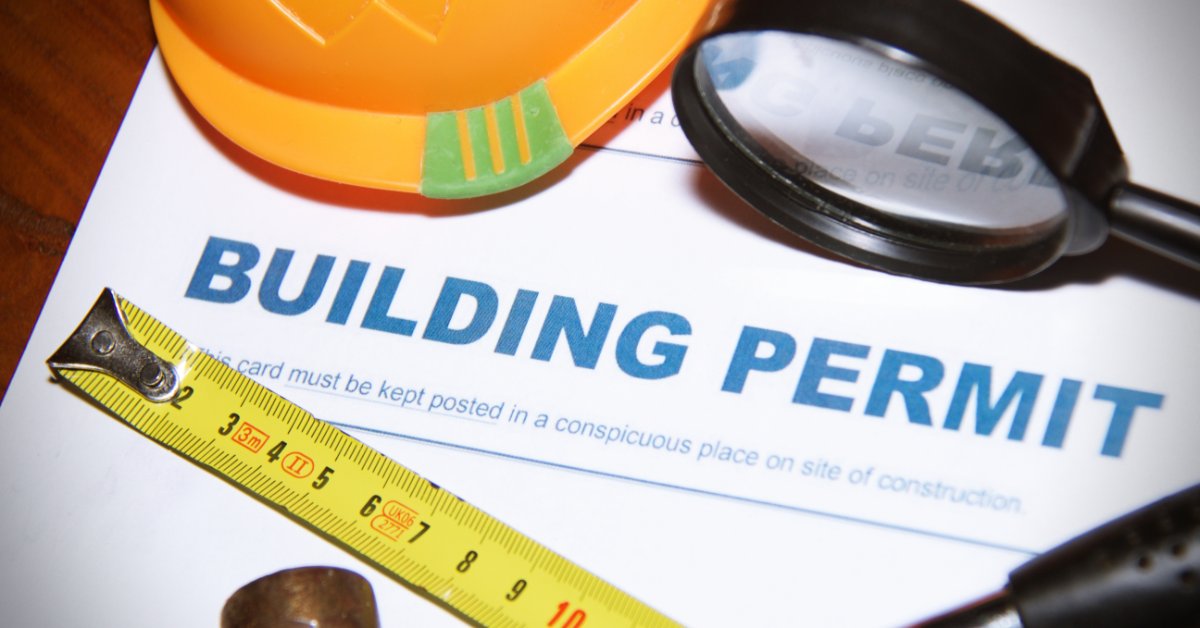 A paper displaying the words “building permit” with a helmet, a measuring tape, and a yellow helmet on top of it.