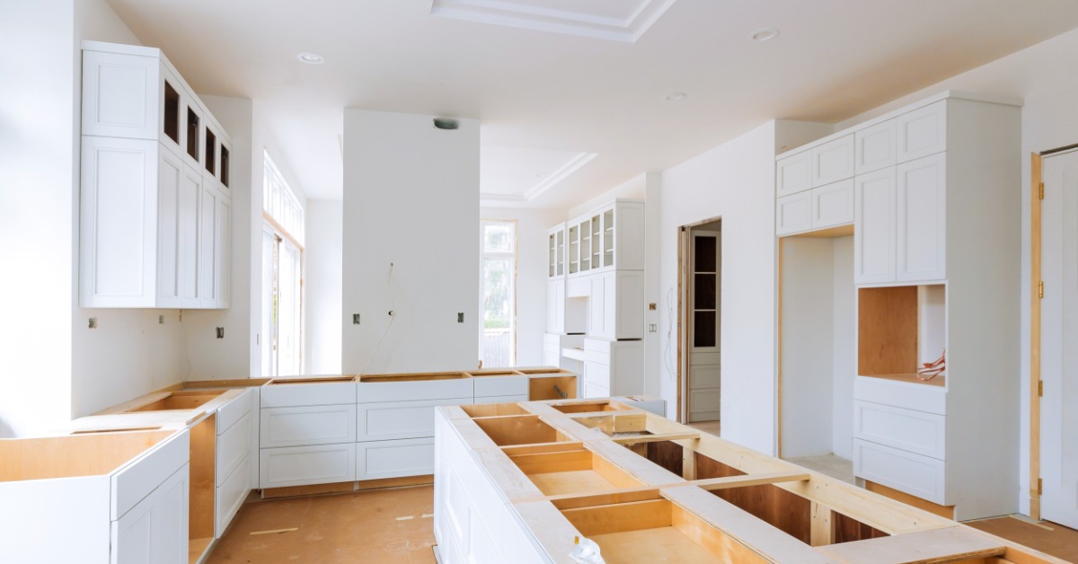 A kitchen under construction with white cabinets and drawers, an island without a counter, and wooden floors.