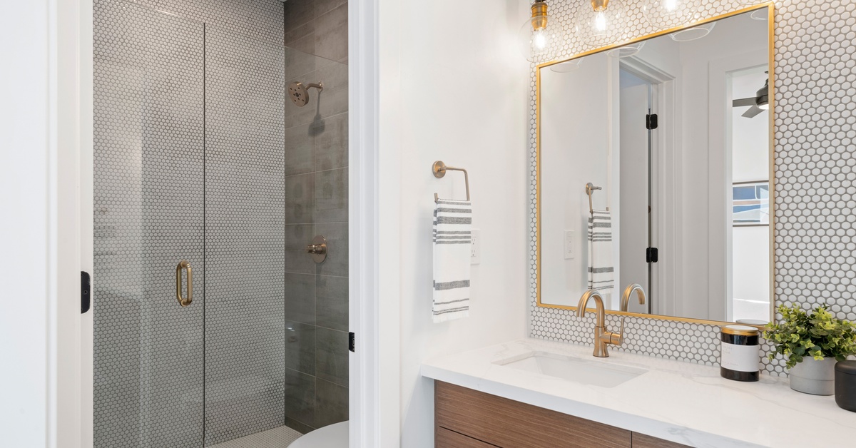 A bathroom with a walk-in shower, a white toilet, and a sink counter with a mirror under a big light fixture.
