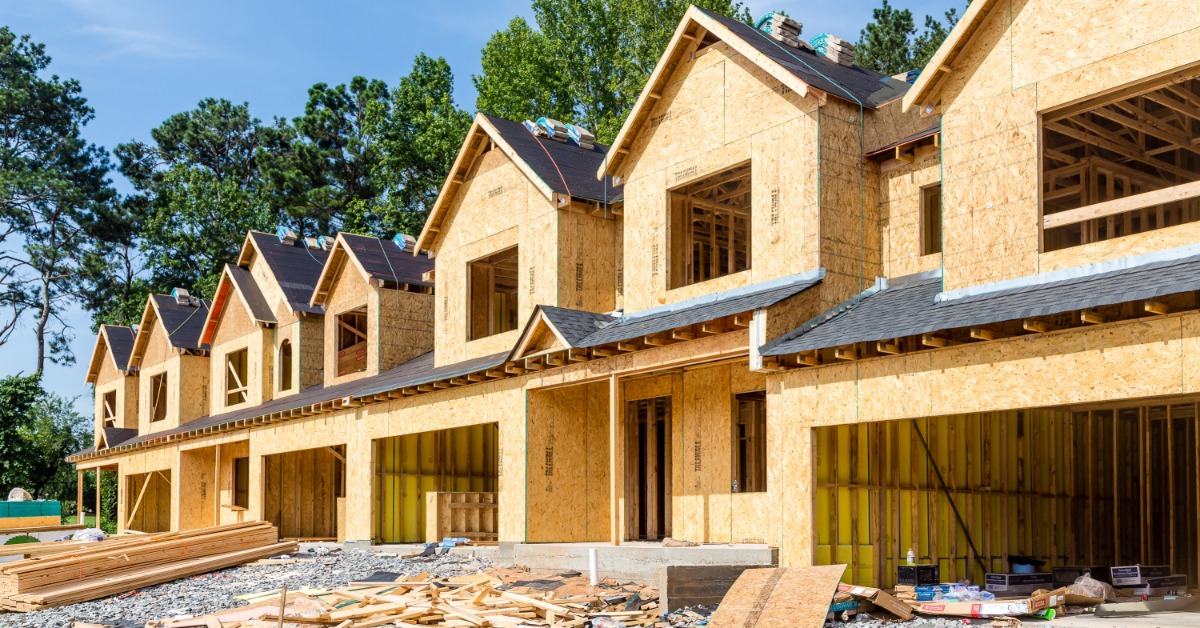 Multiple new two-story home constructions aligned next to each other with multiple trees in the background.
