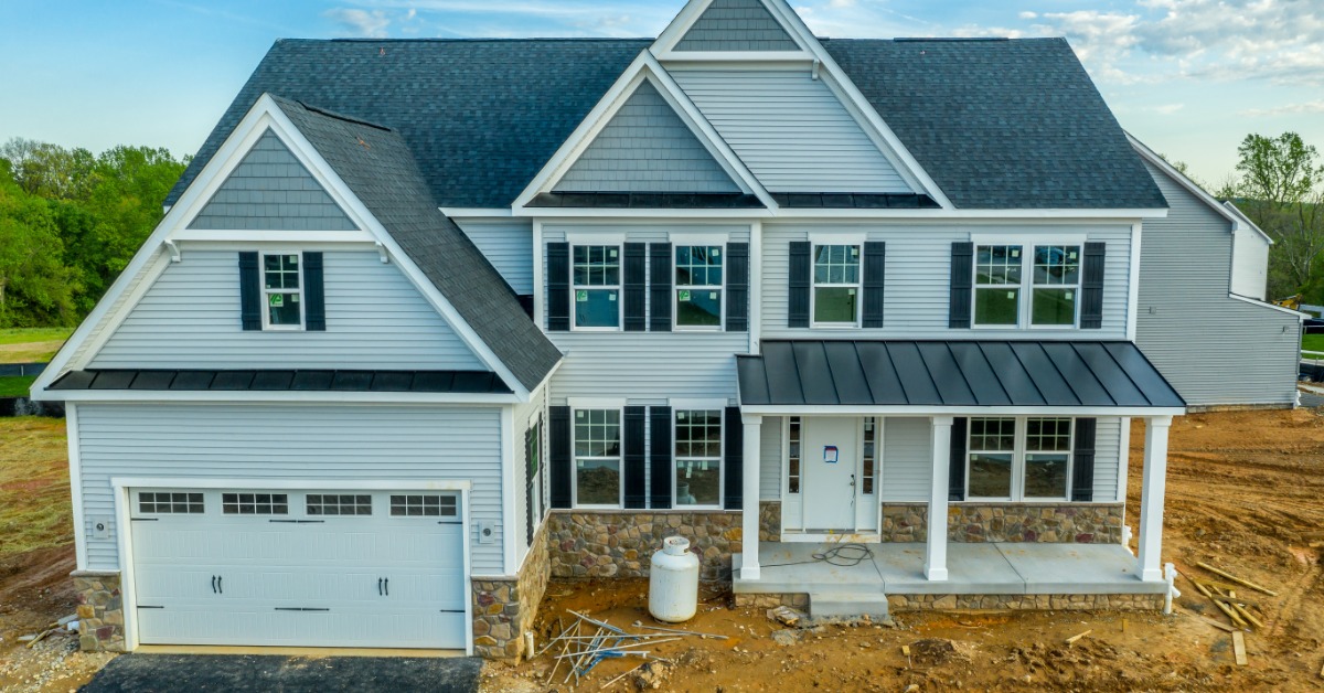 A new construction of a large two-story home with a two-car garage and new windows, on a plot of land covered in dirt.