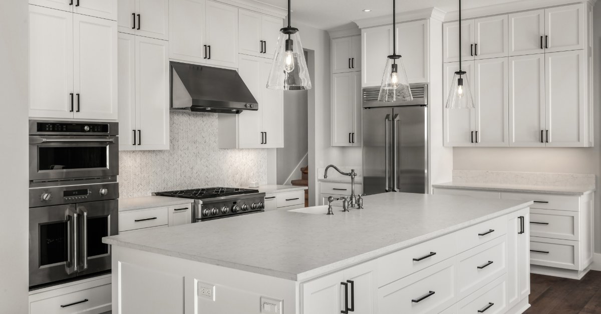 A kitchen with white cabinets, finishes, and doors, black hardware, a large island and stainless steel appliances.