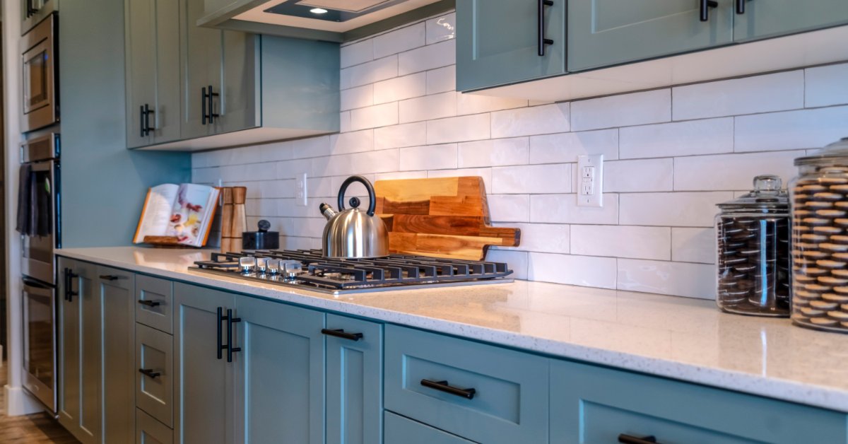 A close-up of multiple kitchen cabinets with a blue color and black hardware, a white countertop, and a large exhaust.