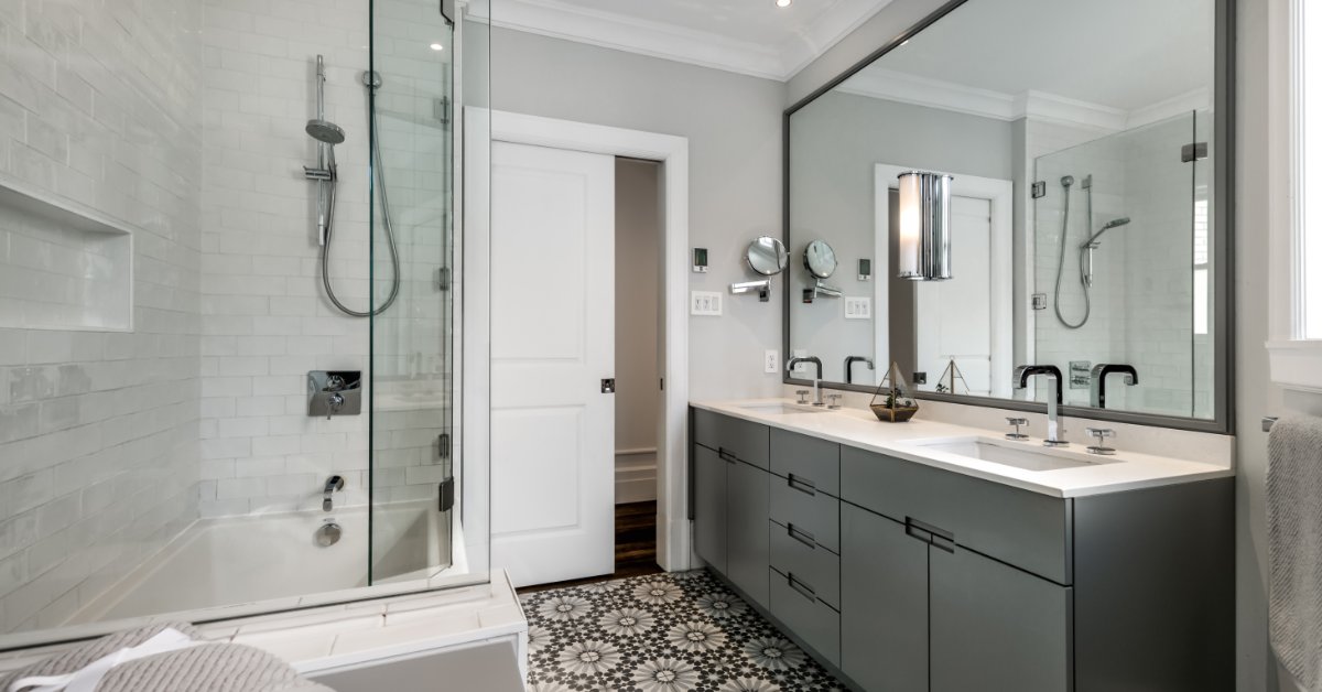 A modern bathroom with flower-tiled floors, double sinks on a long counter, and a large mirror next to a walk-in shower.
