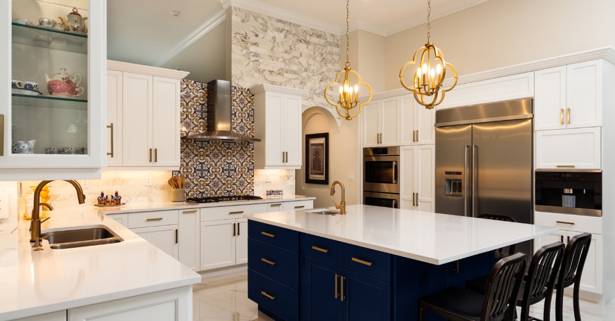 A modern kitchen with gold light fixtures above a blue island, white cabinets, and stainless steel appliances.