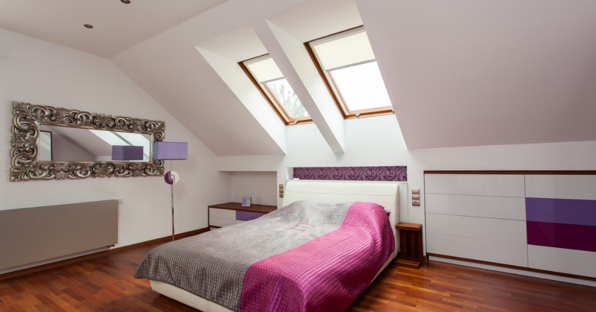 A room with white walls, a sloped ceiling, wooden floors, a queen bed, multiple wall drawers, and two windows.