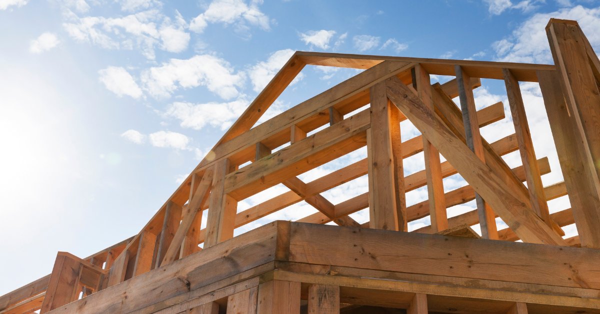 A view from the bottom of the top of a wooden home structure with a triangular end, with the sky in the background.