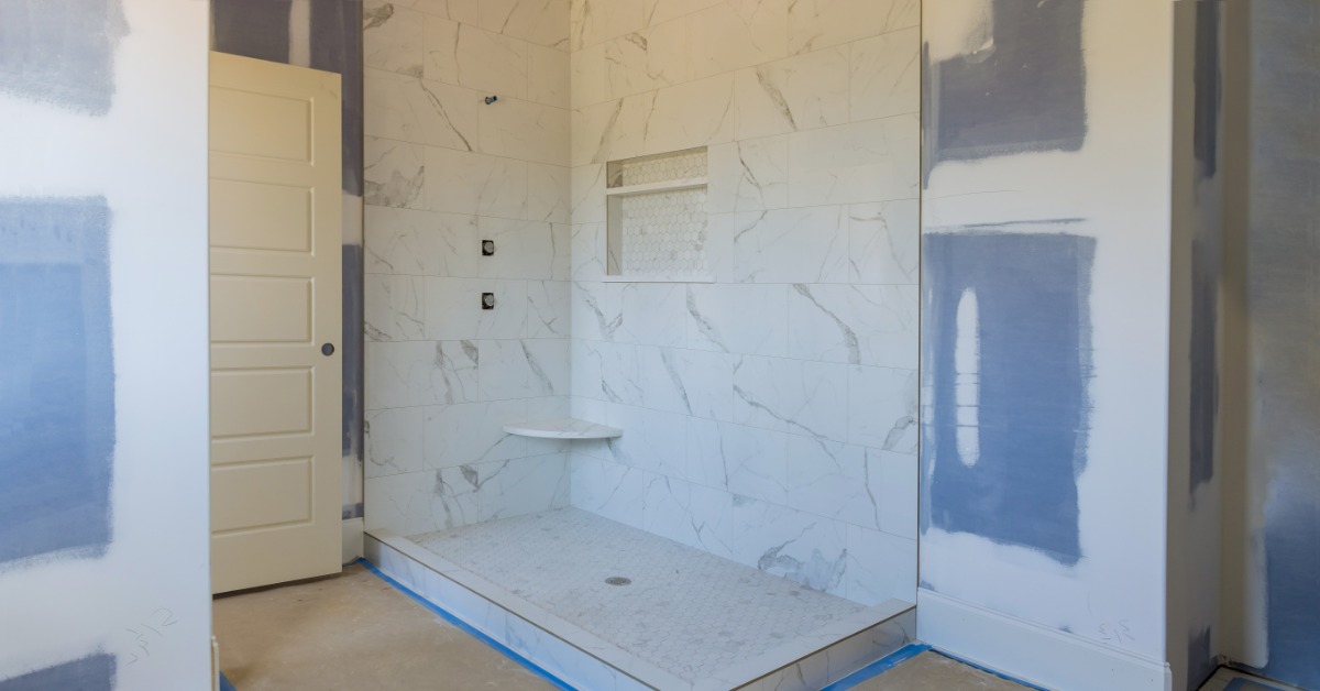 A bathroom undergoing a remodel with a walk-in shower with no panels or faucet, surrounded by blue tape.