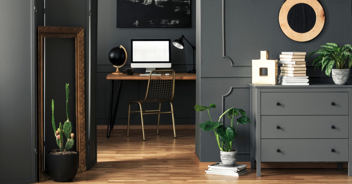 A room with gray walls, grey cabinets, hanging décor, and a wooden desk with a computer monitor in the back.